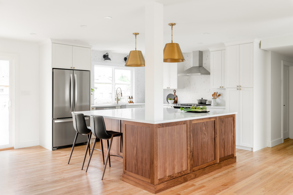 Mid-sized midcentury l-shaped open plan kitchen in Vancouver with an undermount sink, shaker cabinets, dark wood cabinets, quartz benchtops, white splashback, ceramic splashback, stainless steel appliances, light hardwood floors, with island, beige floor and white benchtop.