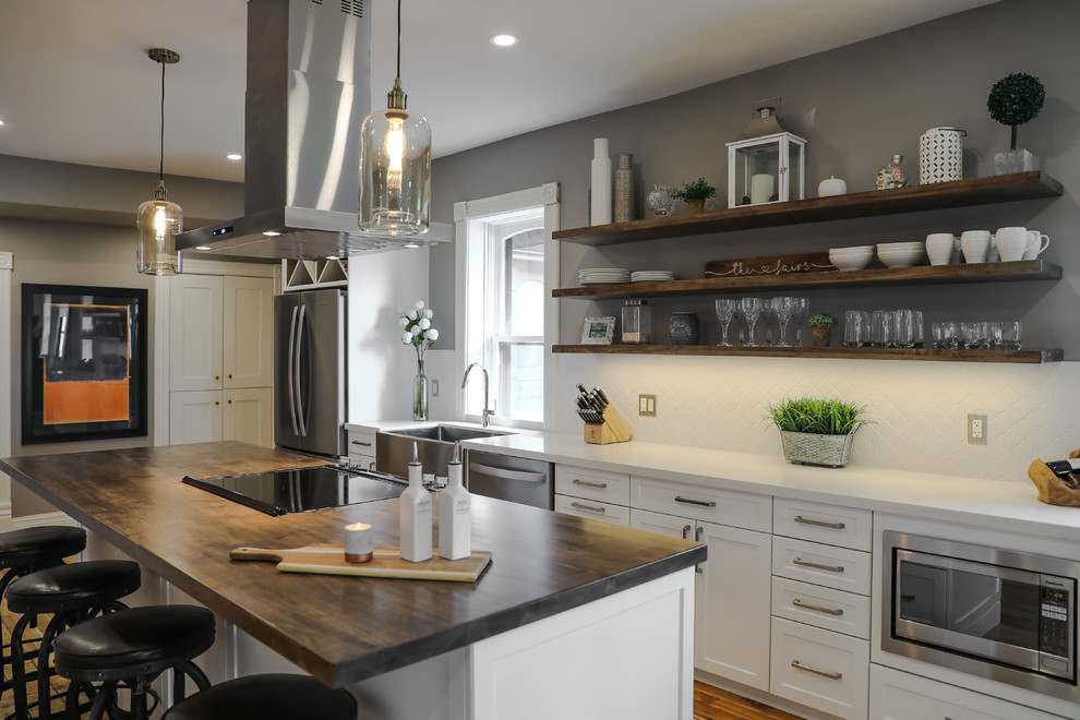 Mid-sized transitional single-wall medium tone wood floor and brown floor eat-in kitchen photo with a farmhouse sink, shaker cabinets, white cabinets, white backsplash, stainless steel appliances, an island and white countertops