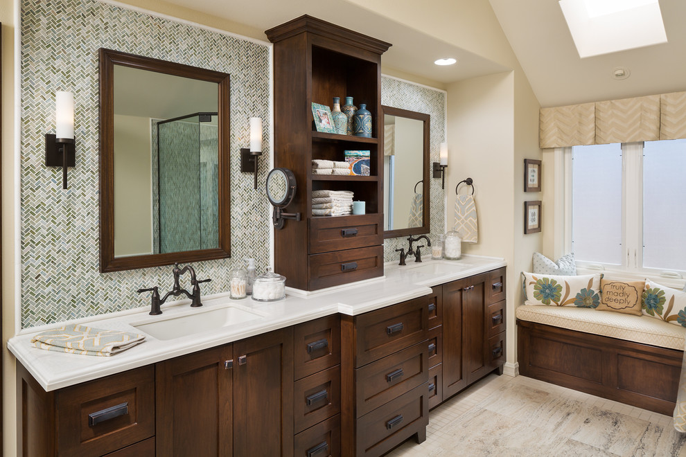 Design ideas for a mid-sized transitional master bathroom in Orange County with shaker cabinets, dark wood cabinets, a drop-in tub, a corner shower, glass tile, beige walls, travertine floors, an undermount sink, marble benchtops, multi-coloured tile, a one-piece toilet, beige floor, a hinged shower door and white benchtops.