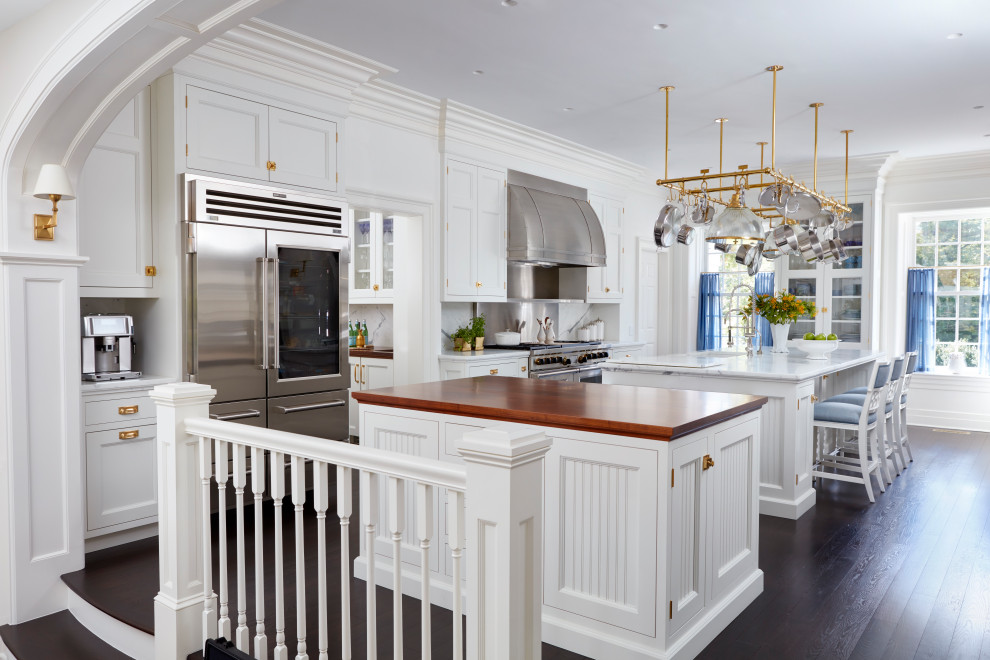 Design ideas for a traditional single-wall open plan kitchen in New York with an undermount sink, recessed-panel cabinets, white cabinets, marble benchtops, white splashback, marble splashback, stainless steel appliances, medium hardwood floors, multiple islands, brown floor and white benchtop.