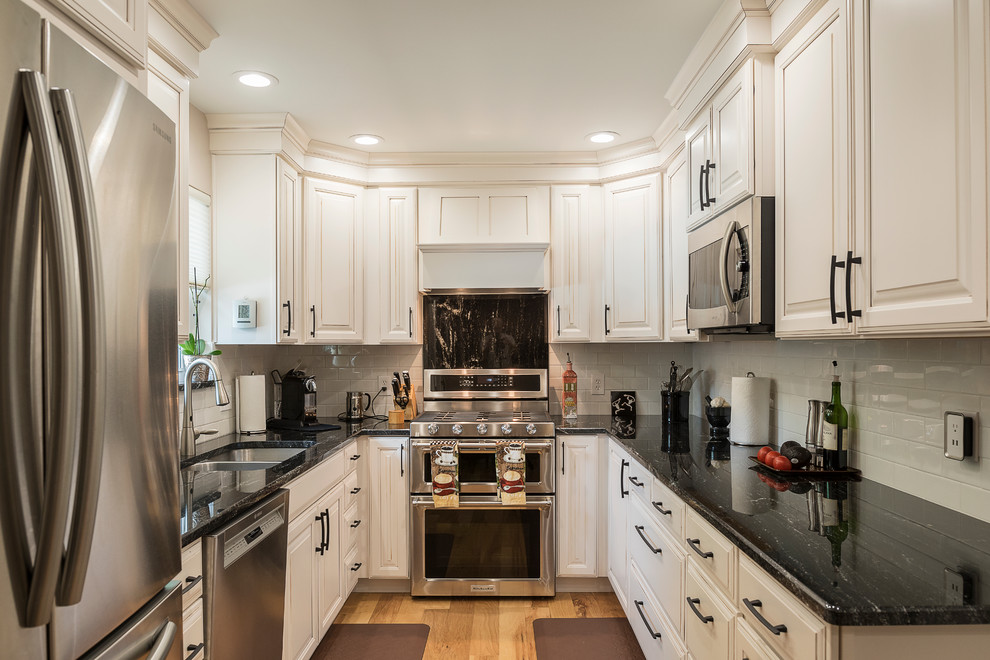 Inspiration for a traditional u-shaped kitchen in Dallas with a double-bowl sink, raised-panel cabinets, white cabinets, yellow splashback, subway tile splashback, stainless steel appliances, no island and brown floor.
