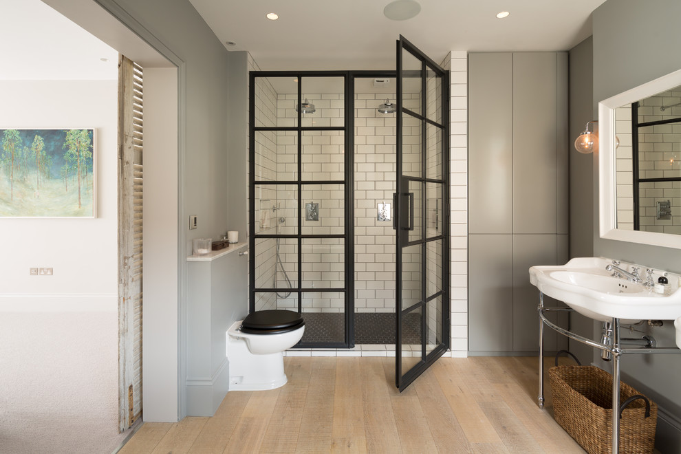 Inspiration for a mid-sized contemporary master bathroom in London with flat-panel cabinets, grey cabinets, a curbless shower, a one-piece toilet, subway tile, grey walls, light hardwood floors, a pedestal sink, beige floor and a hinged shower door.
