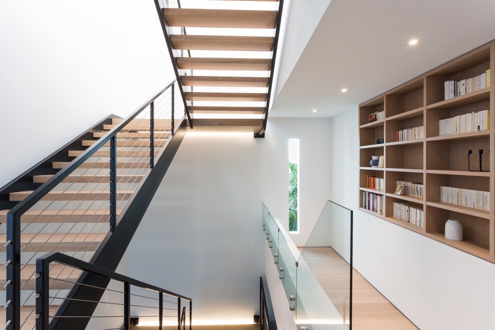 This is an example of a large modern wood floating staircase in Miami with metal risers and metal railing.