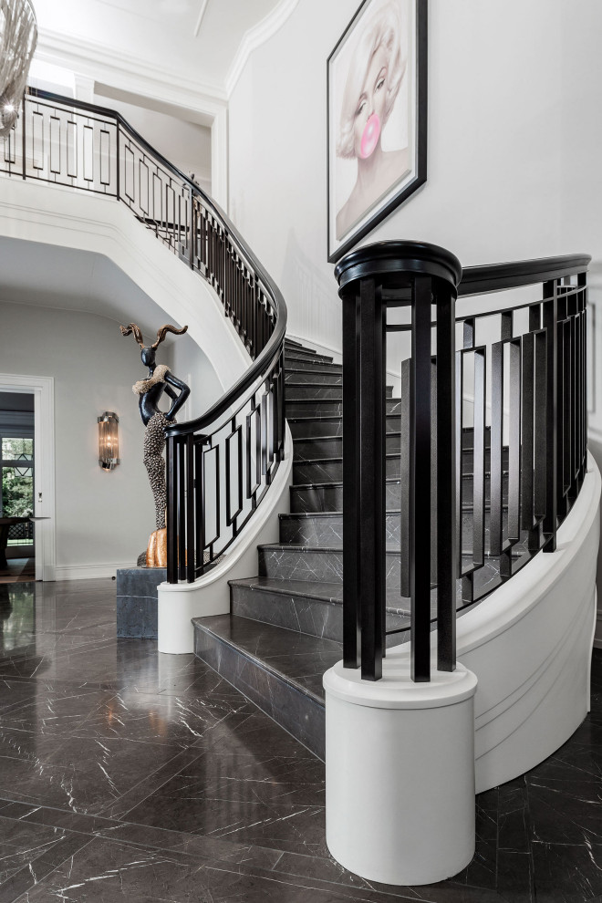 Cette image montre un grand escalier courbe traditionnel en marbre avec des contremarches en marbre et un garde-corps en métal.