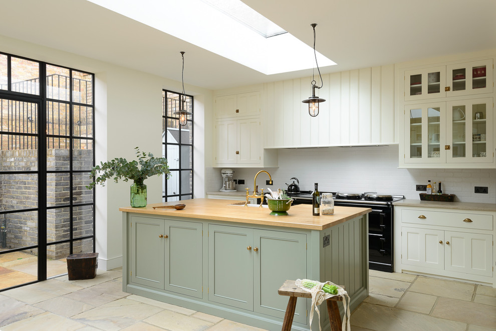 Photo of a large traditional open plan kitchen in London with a farmhouse sink, beaded inset cabinets, green cabinets, wood benchtops, white splashback, subway tile splashback, black appliances and with island.