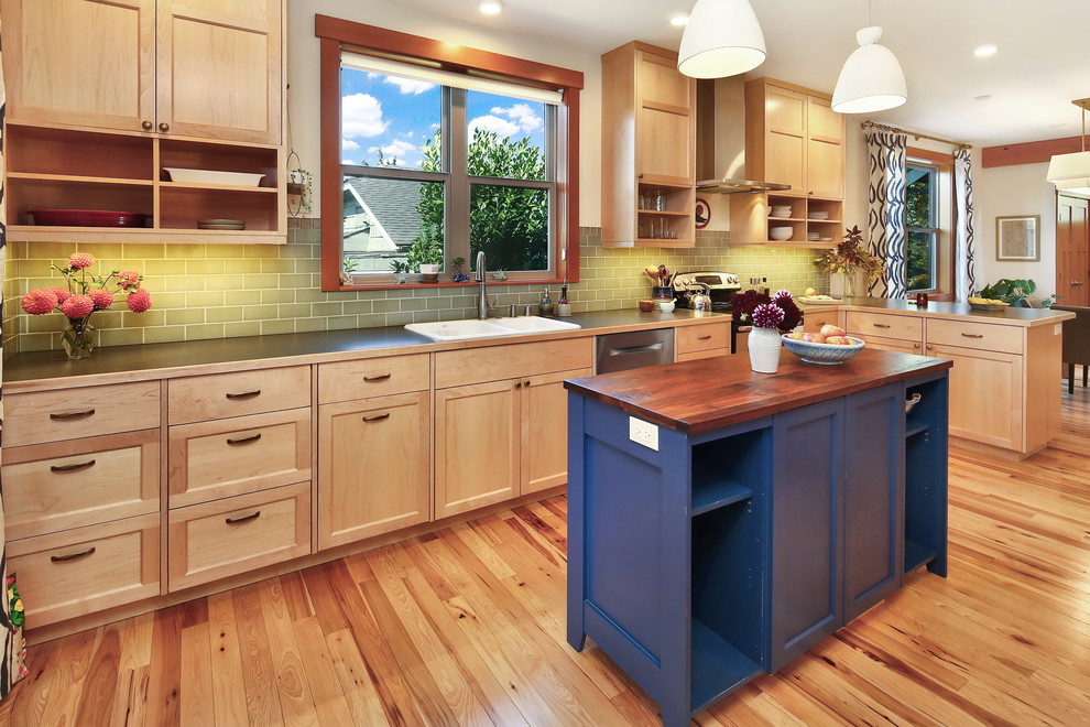 This is an example of an arts and crafts single-wall eat-in kitchen in Seattle with a double-bowl sink, recessed-panel cabinets, light wood cabinets, laminate benchtops, green splashback, subway tile splashback, stainless steel appliances, light hardwood floors, with island and black benchtop.