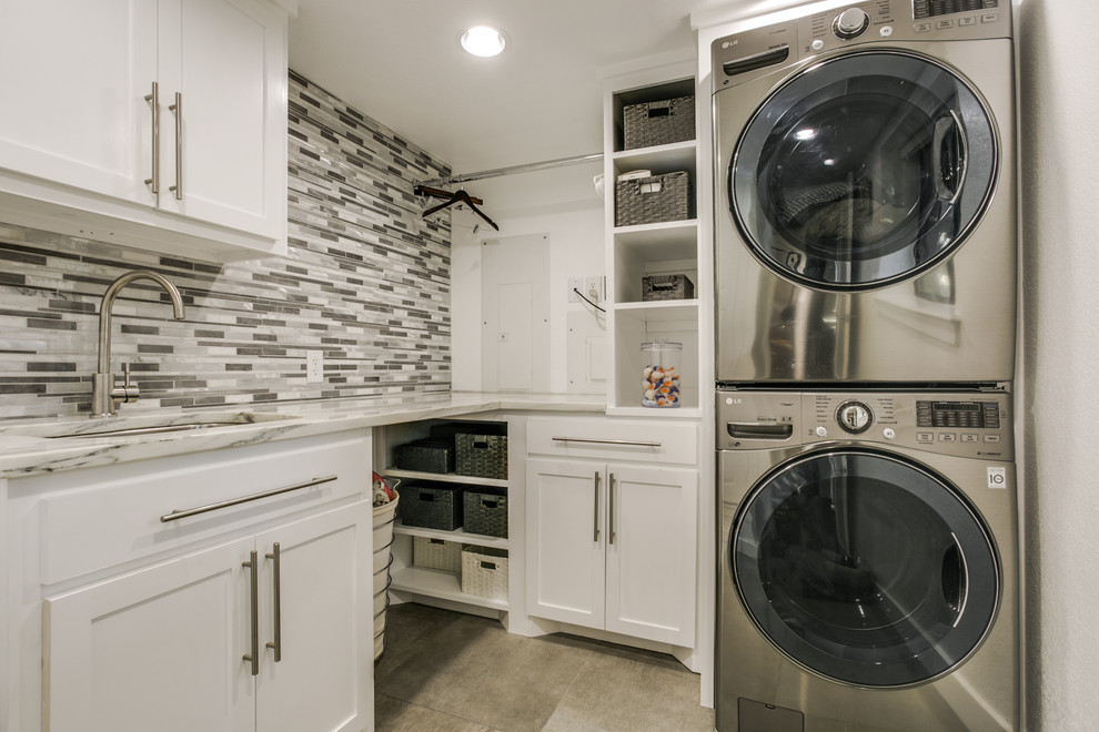 Photo of a contemporary l-shaped laundry room in Dallas with an undermount sink, shaker cabinets, white cabinets, quartzite benchtops, grey walls, a stacked washer and dryer and grey floor.