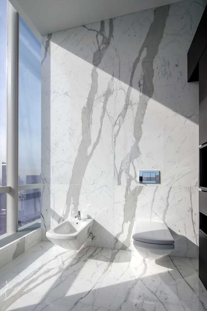 This is an example of an expansive modern master bathroom in New York with flat-panel cabinets, black cabinets, a drop-in tub, a double shower, a wall-mount toilet, white tile, stone tile, white walls, marble floors, an undermount sink and marble benchtops.