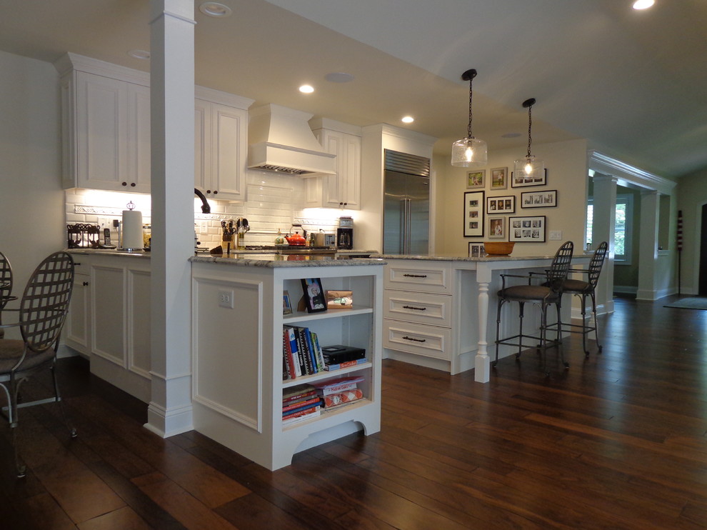 Large transitional u-shaped dark wood floor open concept kitchen photo in Raleigh with a farmhouse sink, recessed-panel cabinets, white cabinets, granite countertops, white backsplash, subway tile backsplash, stainless steel appliances and an island