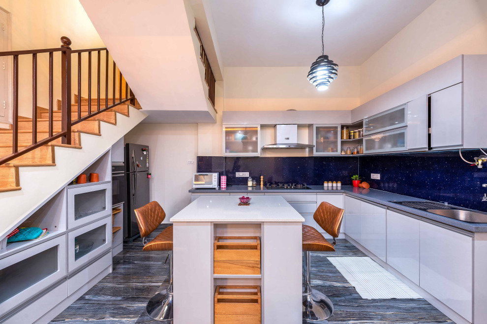 This is an example of a large contemporary l-shaped kitchen in Bengaluru with a drop-in sink, flat-panel cabinets, grey cabinets, blue splashback, black appliances, with island, multi-coloured floor and grey benchtop.