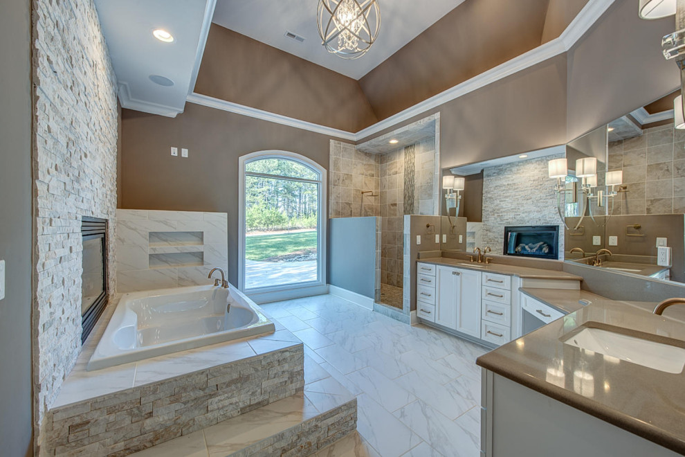 Inspiration for an expansive transitional master bathroom in Charlotte with white cabinets, a drop-in tub, a corner shower, multi-coloured tile, stone tile, brown walls, ceramic floors, an undermount sink, granite benchtops, white floor, an open shower, beige benchtops, a niche, a double vanity and a built-in vanity.