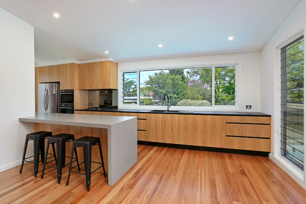 Inspiration for a large contemporary galley kitchen pantry in Sydney with a drop-in sink, flat-panel cabinets, light wood cabinets, quartz benchtops, black splashback, glass sheet splashback, stainless steel appliances, light hardwood floors, a peninsula and yellow floor.
