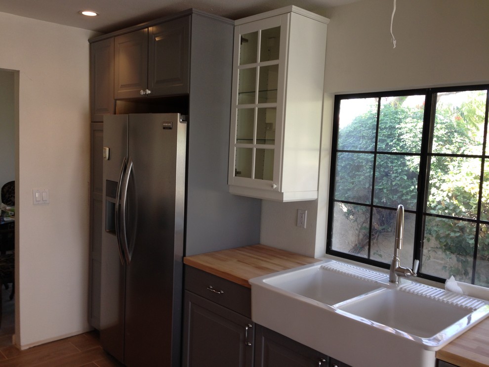 Enclosed kitchen - transitional u-shaped laminate floor and brown floor enclosed kitchen idea with a farmhouse sink, glass-front cabinets, white cabinets, wood countertops, white backsplash, subway tile backsplash and stainless steel appliances