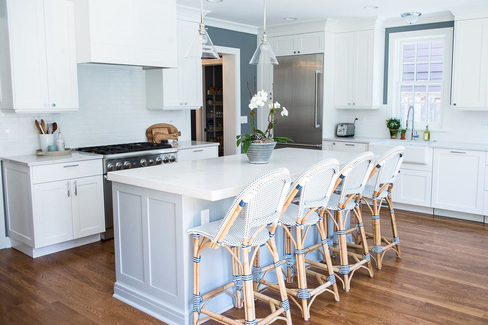 Inspiration for a large transitional l-shaped medium tone wood floor and brown floor open concept kitchen remodel in Chicago with a farmhouse sink, recessed-panel cabinets, white cabinets, quartz countertops, white backsplash, subway tile backsplash, stainless steel appliances, an island and white countertops