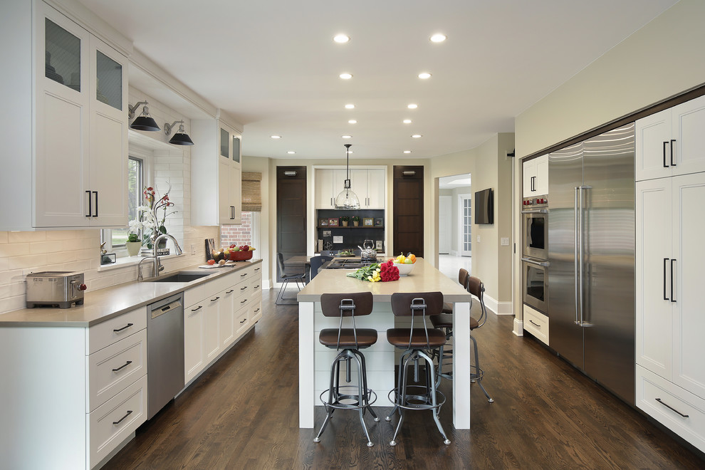 Inspiration for a large industrial u-shaped eat-in kitchen in Chicago with an undermount sink, recessed-panel cabinets, white cabinets, quartzite benchtops, white splashback, cement tile splashback, stainless steel appliances, dark hardwood floors, with island, brown floor and beige benchtop.
