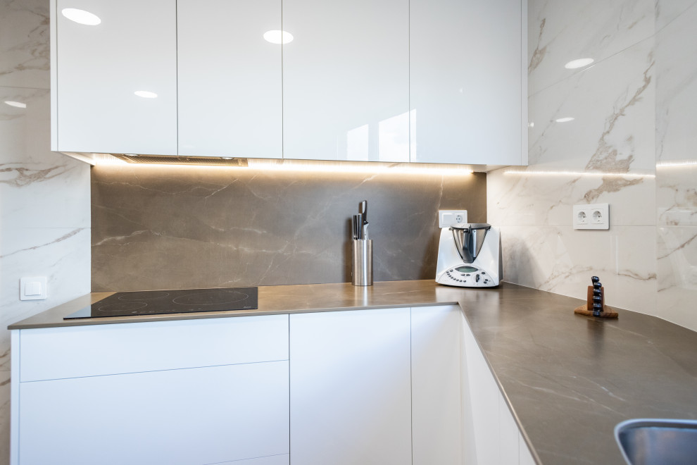This is an example of a large modern l-shaped separate kitchen in Barcelona with a single-bowl sink, flat-panel cabinets, white cabinets, white splashback, ceramic splashback, stainless steel appliances, terrazzo floors, no island, brown floor and grey benchtop.