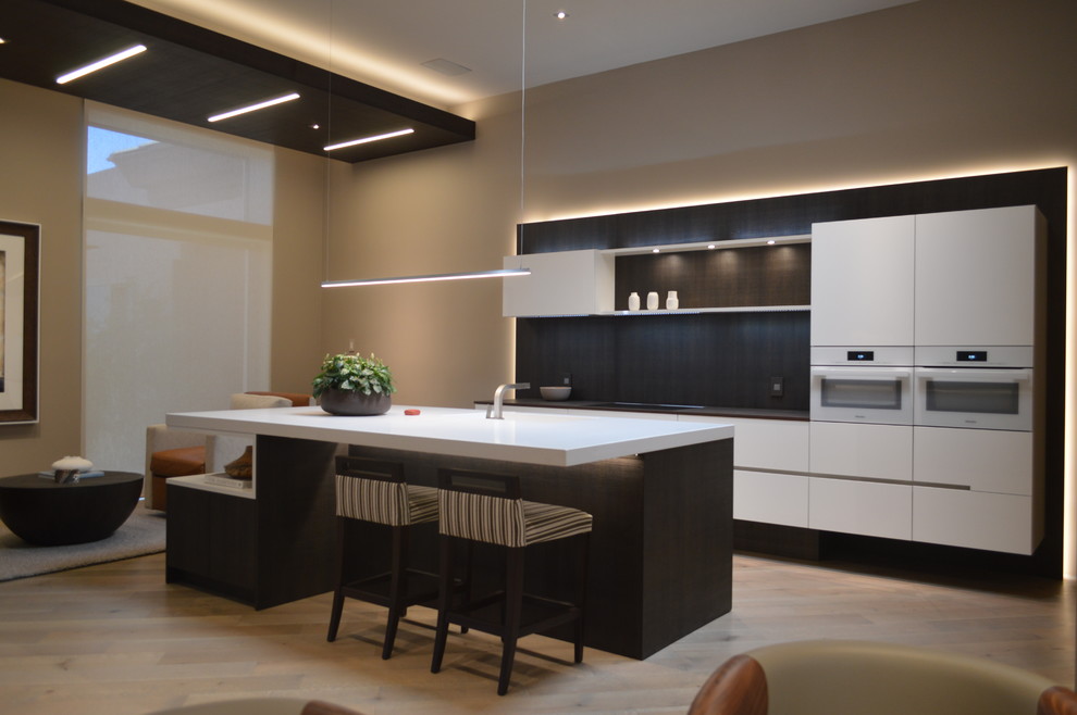 Example of a mid-sized minimalist galley light wood floor and brown floor open concept kitchen design in Phoenix with a single-bowl sink, white cabinets, black backsplash, white appliances, an island and flat-panel cabinets