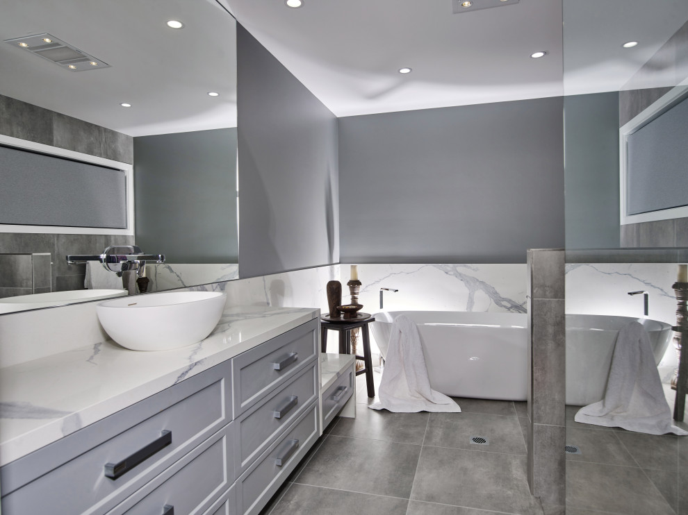 Свежая идея для дизайна: большая главная, серо-белая ванная комната в стиле модернизм с фасадами с утопленной филенкой, серыми фасадами, отдельно стоящей ванной, угловым душем, унитазом-моноблоком, плиткой из известняка, серыми стенами, полом из известняка, настольной раковиной, столешницей из известняка, серым полом, душем с распашными дверями, белой столешницей, тумбой под одну раковину, подвесной тумбой и сводчатым потолком - отличное фото интерьера