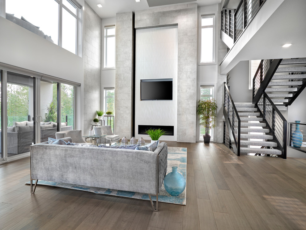 This is an example of a large contemporary open concept living room in Edmonton with grey walls, medium hardwood floors, a ribbon fireplace, a tile fireplace surround, a built-in media wall and brown floor.
