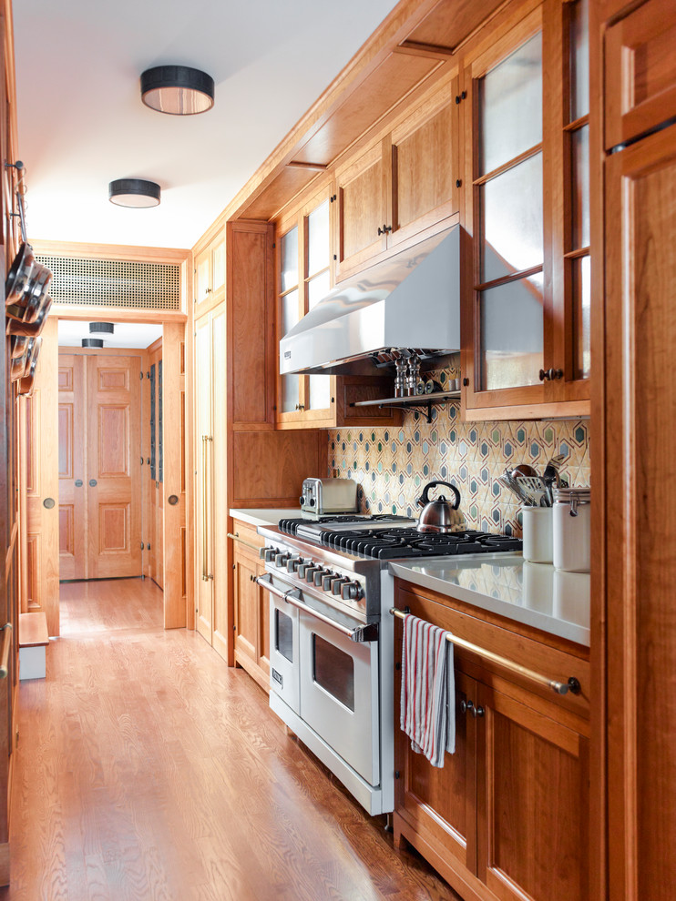 Arts and crafts galley kitchen in New York with recessed-panel cabinets, medium wood cabinets, multi-coloured splashback, stainless steel appliances, medium hardwood floors and no island.