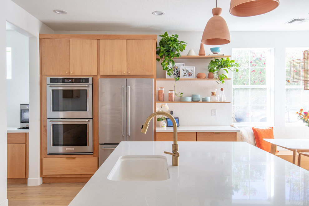 Photo of a mid-sized midcentury u-shaped eat-in kitchen in Phoenix with an undermount sink, flat-panel cabinets, light wood cabinets, quartz benchtops, white splashback, stainless steel appliances, light hardwood floors, with island, brown floor and white benchtop.