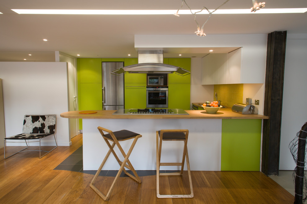 Mid-sized galley open plan kitchen in Paris with a double-bowl sink, beaded inset cabinets, green cabinets, wood benchtops, yellow splashback, glass tile splashback, stainless steel appliances, slate floors, with island and black floor.