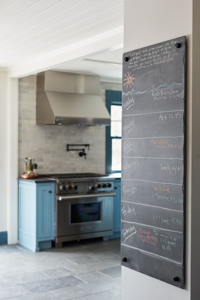 Mid-sized farmhouse single-wall slate floor and gray floor eat-in kitchen photo in Boston with recessed-panel cabinets, blue cabinets, limestone countertops, gray backsplash, stainless steel appliances and an island