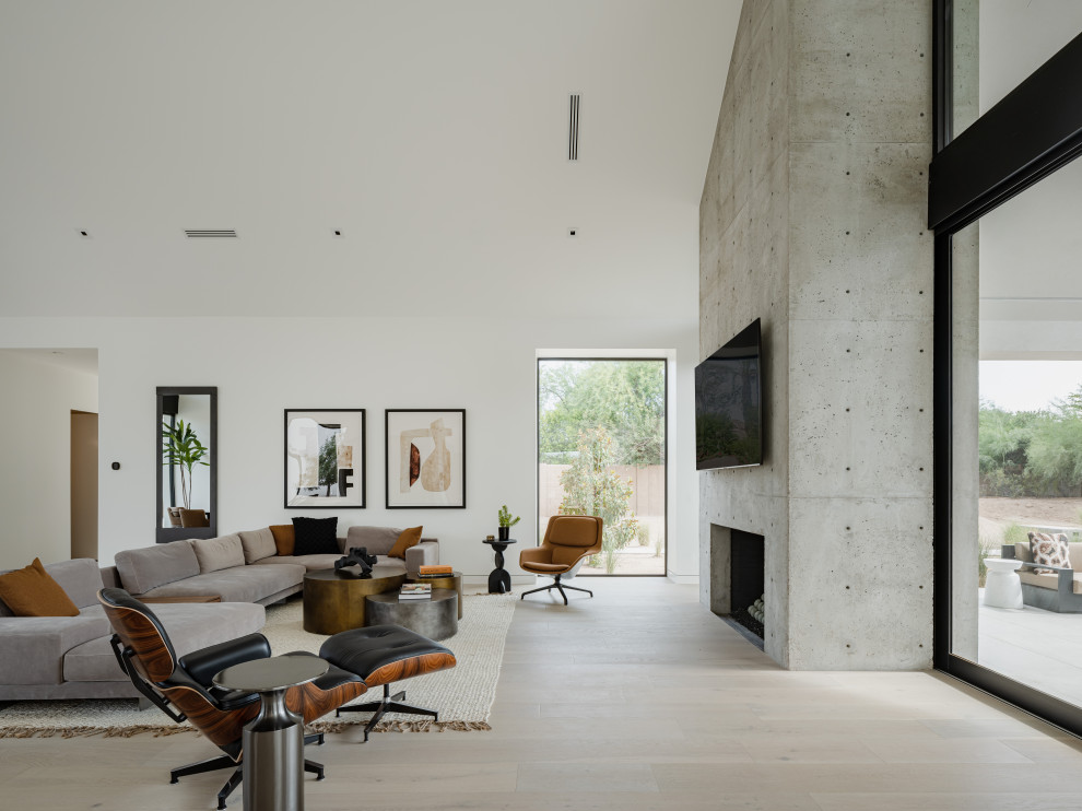 Свежая идея для дизайна: открытая гостиная комната в стиле модернизм с белыми стенами, светлым паркетным полом, стандартным камином, фасадом камина из бетона, телевизором на стене и сводчатым потолком - отличное фото интерьера