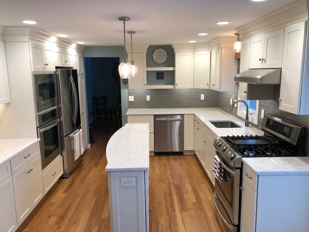 This is an example of a large transitional l-shaped separate kitchen in New York with an undermount sink, shaker cabinets, white cabinets, quartzite benchtops, grey splashback, glass tile splashback, stainless steel appliances, medium hardwood floors, with island, multi-coloured floor and white benchtop.