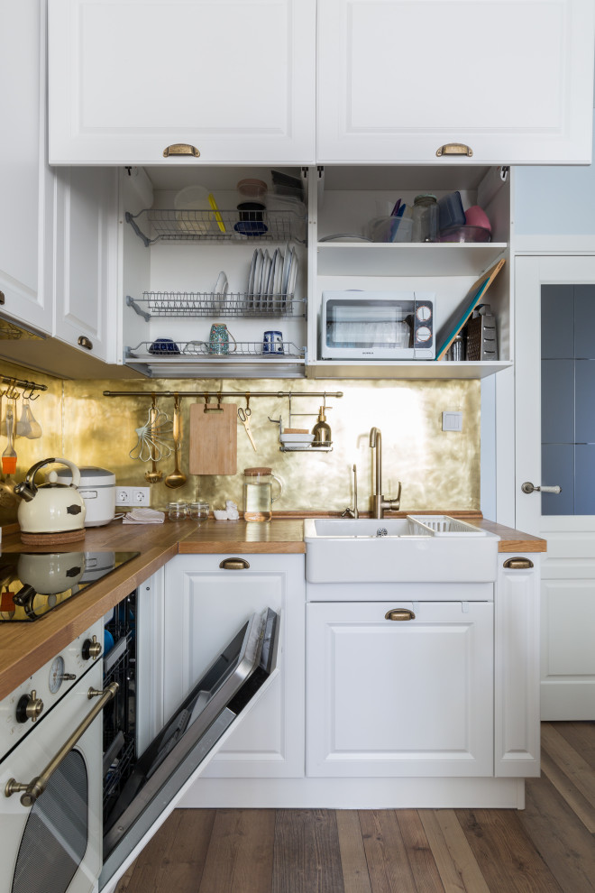 Small eclectic l-shaped kitchen/diner in Other with a belfast sink, wood worktops, metallic splashback, metal splashback, white appliances, laminate floors, no island, brown floors, brown worktops and a feature wall.