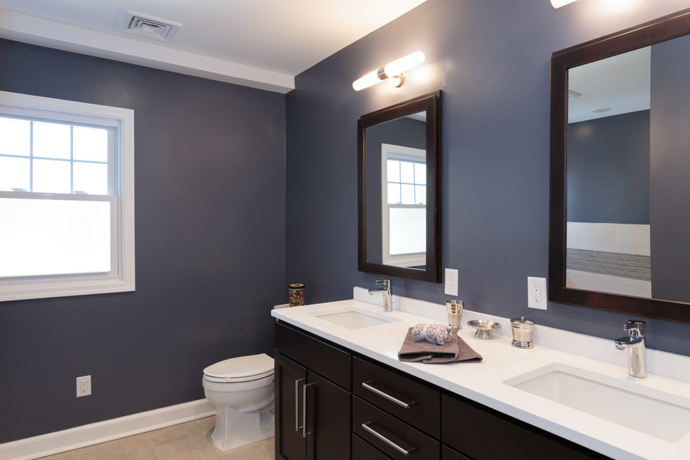Photo of a large contemporary master bathroom in New York with an undermount sink, recessed-panel cabinets, dark wood cabinets, engineered quartz benchtops, an alcove tub, a corner shower, a two-piece toilet, gray tile, ceramic tile, blue walls and ceramic floors.