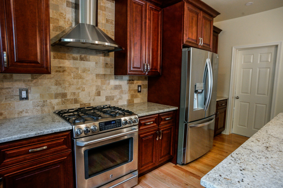 Bild på ett beige beige kök, med en undermonterad diskho, luckor med upphöjd panel, röda skåp, granitbänkskiva, beige stänkskydd, stänkskydd i stenkakel, ljust trägolv, en köksö och gult golv