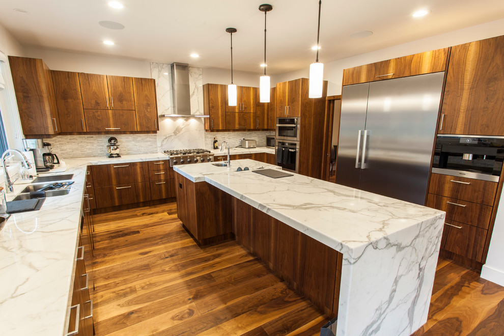 This is an example of a large contemporary u-shaped open plan kitchen in Edmonton with a double-bowl sink, flat-panel cabinets, medium wood cabinets, marble benchtops, grey splashback, matchstick tile splashback, stainless steel appliances, medium hardwood floors and with island.