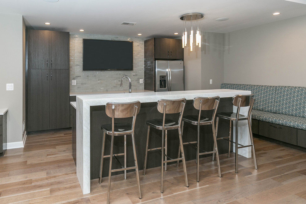 This is an example of a mid-sized contemporary galley seated home bar in Detroit with an undermount sink, flat-panel cabinets, medium wood cabinets, quartz benchtops, beige splashback, subway tile splashback, light hardwood floors and beige floor.