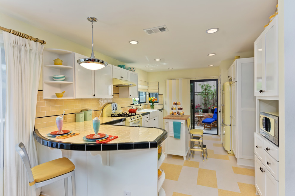 Inspiration for a mid-sized traditional l-shaped kitchen in San Diego with a farmhouse sink, shaker cabinets, white cabinets, tile benchtops, yellow splashback, subway tile splashback, coloured appliances, linoleum floors, with island, multi-coloured floor and yellow benchtop.