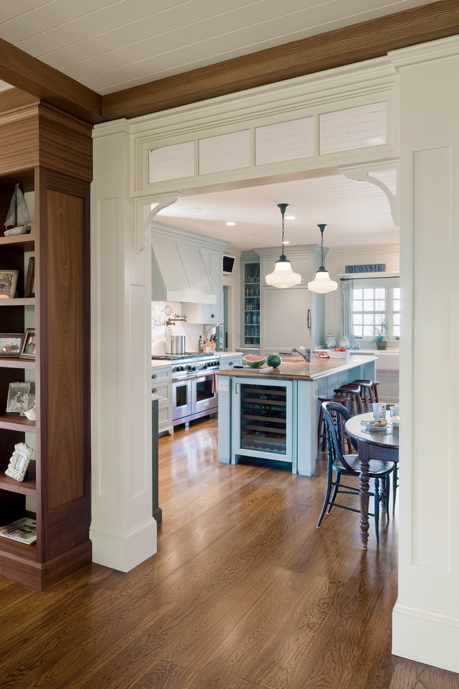 This is an example of a large beach style u-shaped eat-in kitchen in Providence with a farmhouse sink, shaker cabinets, grey cabinets, wood benchtops, white splashback, panelled appliances, medium hardwood floors and with island.