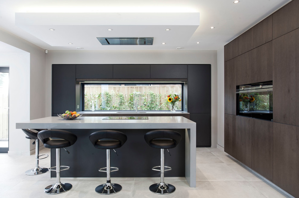 Inspiration for a mid-sized contemporary l-shaped eat-in kitchen in Belfast with a double-bowl sink, flat-panel cabinets, black cabinets, quartzite benchtops, black appliances, with island, window splashback, grey floor and grey benchtop.