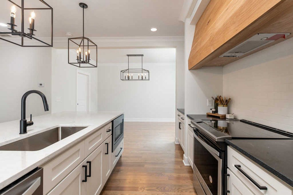 Example of a large transitional galley medium tone wood floor and brown floor open concept kitchen design with an undermount sink, shaker cabinets, white cabinets, quartz countertops, white backsplash, ceramic backsplash, stainless steel appliances, an island and white countertops