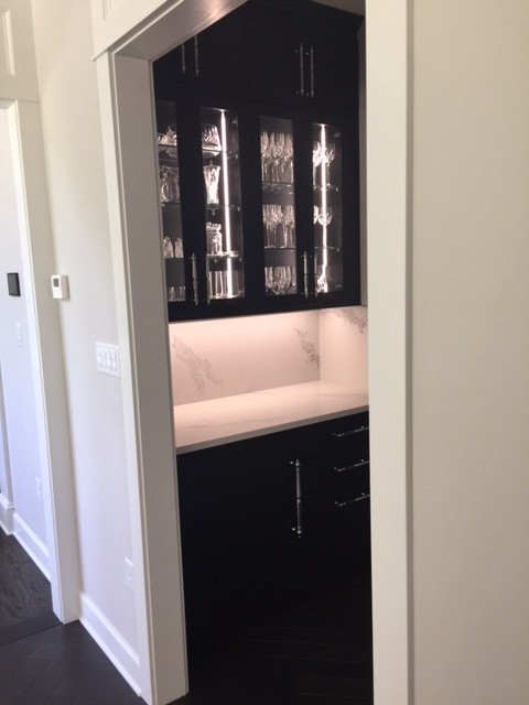 Inspiration for a large transitional u-shaped vinyl floor and black floor kitchen pantry remodel with a farmhouse sink, recessed-panel cabinets, white backsplash, paneled appliances, an island, white countertops, black cabinets, quartz countertops and quartz backsplash