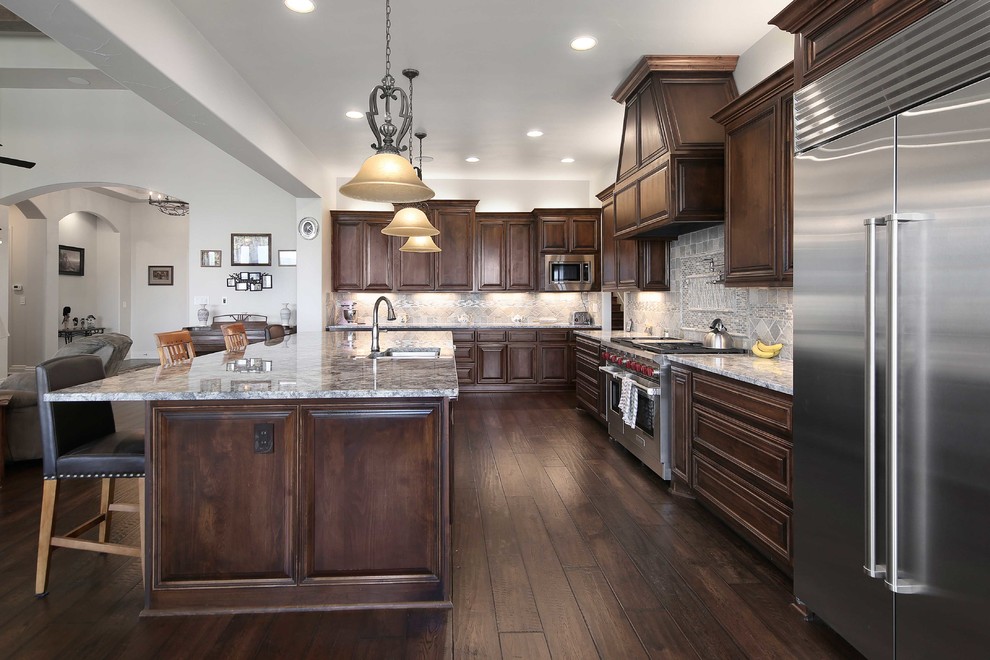Inspiration for a large traditional eat-in kitchen in Austin with recessed-panel cabinets, dark wood cabinets, granite benchtops, grey splashback, ceramic splashback, stainless steel appliances, dark hardwood floors and with island.