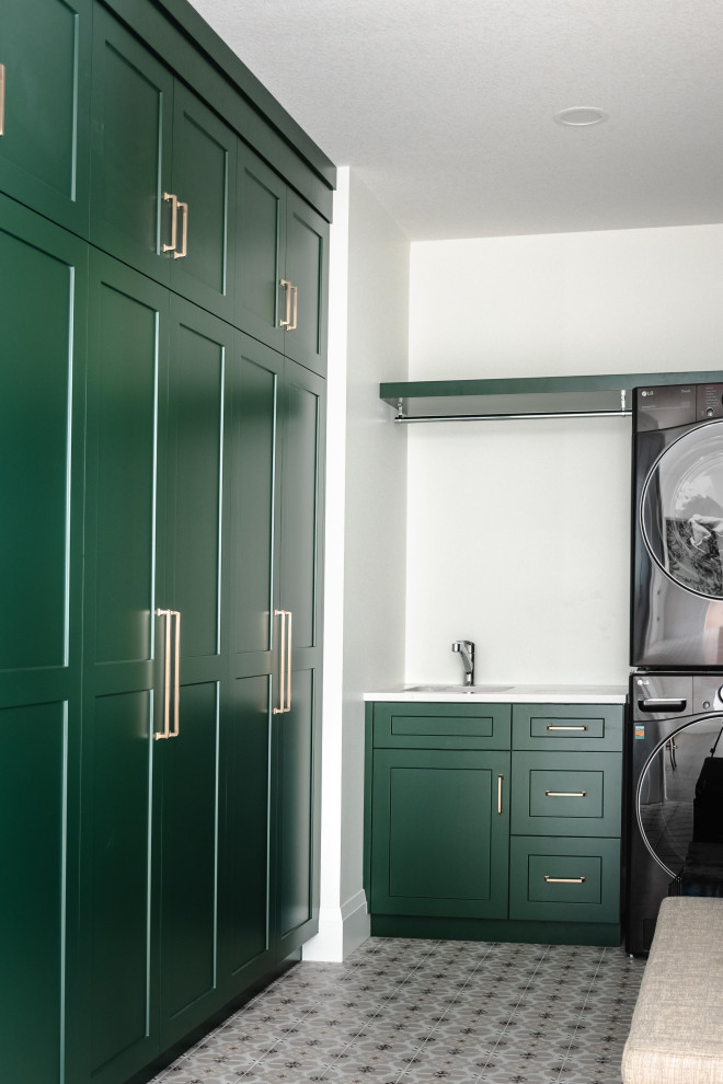Imagen de cuarto de lavado en L minimalista grande con fregadero bajoencimera, puertas de armario verdes, encimera de cuarzo compacto, paredes blancas, lavadora y secadora apiladas y encimeras blancas