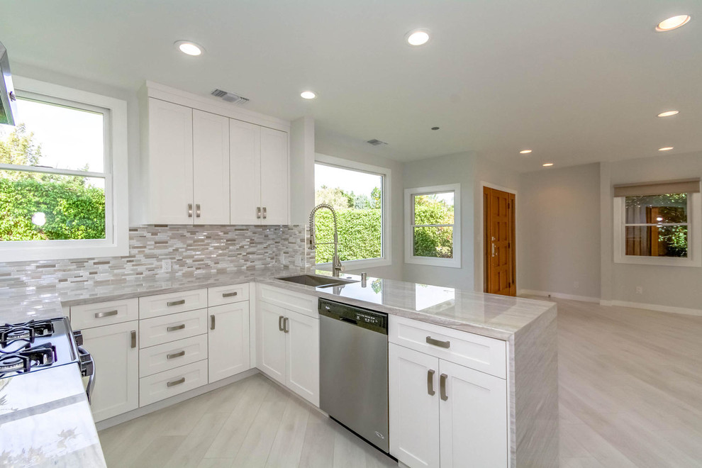 Open concept kitchen - mid-sized transitional u-shaped porcelain tile open concept kitchen idea in Los Angeles with a double-bowl sink, shaker cabinets, white cabinets, quartz countertops, beige backsplash, matchstick tile backsplash, stainless steel appliances and an island