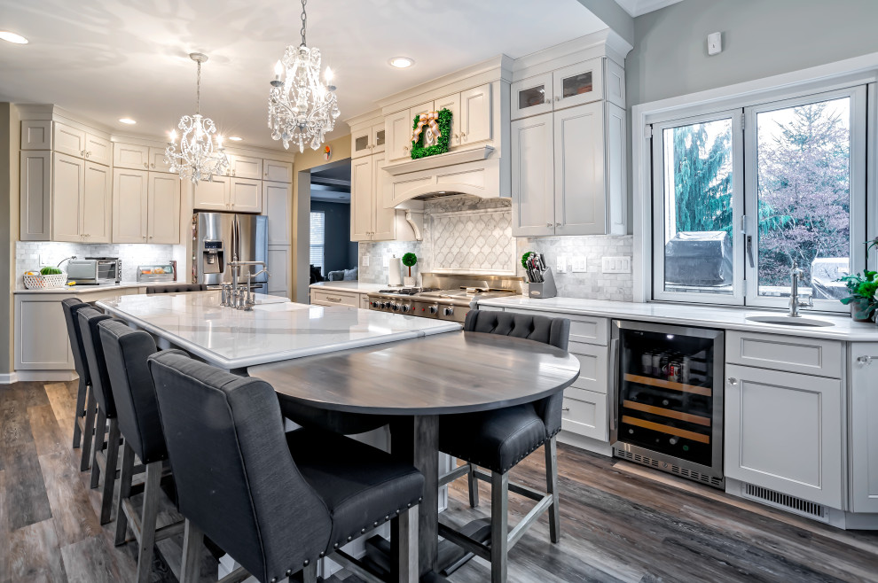 Example of a large transitional single-wall medium tone wood floor and brown floor eat-in kitchen design in Philadelphia with a farmhouse sink, shaker cabinets, white cabinets, quartz countertops, gray backsplash, porcelain backsplash, stainless steel appliances, an island and white countertops