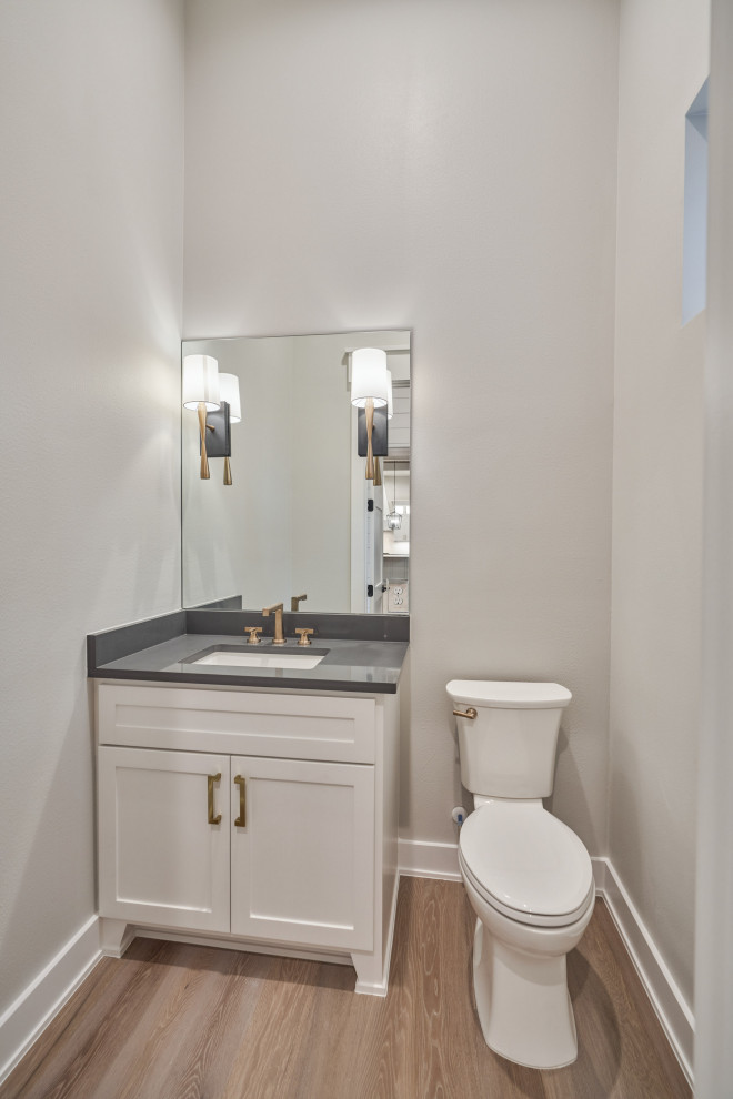 Aménagement d'un WC et toilettes craftsman de taille moyenne avec un placard avec porte à panneau encastré, des portes de placard blanches, WC à poser, un mur blanc, un sol en bois brun, un lavabo encastré, un sol marron, un plan de toilette gris et meuble-lavabo encastré.
