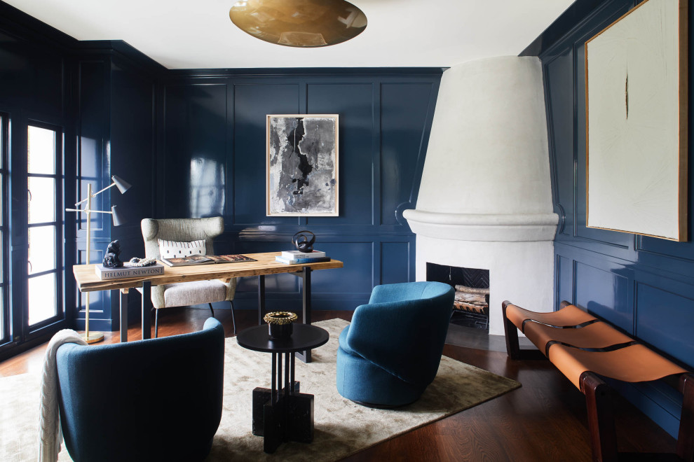 Klassisches Arbeitszimmer mit Studio, blauer Wandfarbe, dunklem Holzboden, Eckkamin, verputzter Kaminumrandung, freistehendem Schreibtisch, braunem Boden und Wandpaneelen in Los Angeles