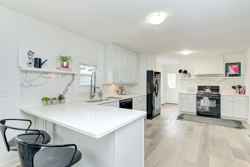 Mid-sized contemporary l-shaped eat-in kitchen in Indianapolis with a single-bowl sink, flat-panel cabinets, white cabinets, solid surface benchtops, white splashback, marble splashback, black appliances, light hardwood floors, a peninsula, beige floor and white benchtop.