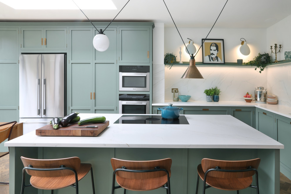 Inspiration for a mid-sized transitional l-shaped eat-in kitchen in London with an integrated sink, shaker cabinets, green cabinets, quartzite benchtops, white splashback, engineered quartz splashback, stainless steel appliances, medium hardwood floors, with island, brown floor and white benchtop.