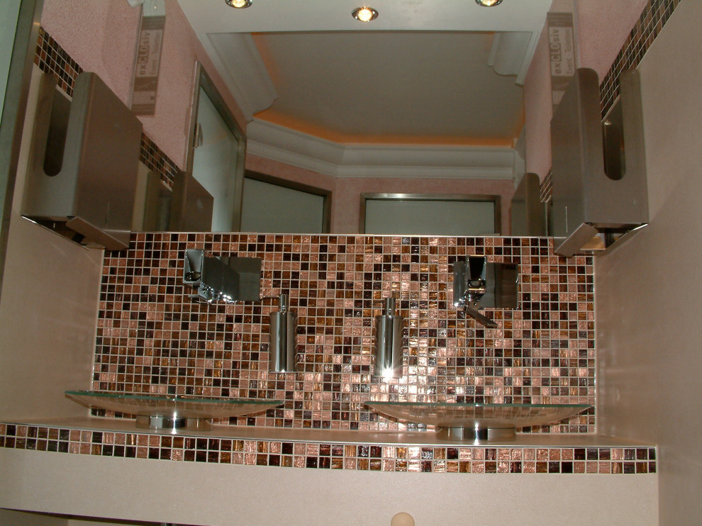 Cette image montre un grand WC suspendu traditionnel avec un carrelage marron, un carrelage en pâte de verre, un mur beige, un sol en linoléum, une vasque, un plan de toilette en verre, un sol orange, un plan de toilette beige et meuble-lavabo suspendu.