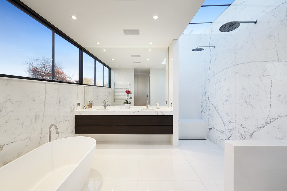 Photo of a modern master bathroom in Melbourne with dark wood cabinets, a freestanding tub, a double shower, a wall-mount toilet, porcelain tile, white walls, porcelain floors, an undermount sink, marble benchtops and white tile.