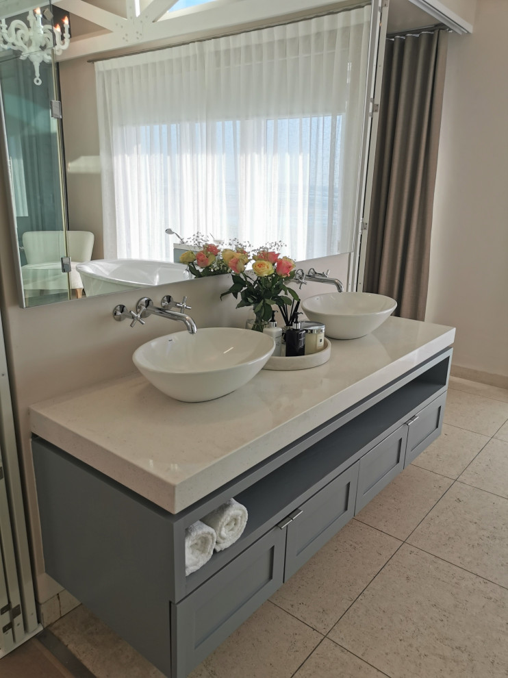 Photo of an expansive beach style master bathroom in London with grey cabinets, a freestanding tub, a wall-mount toilet, an enclosed toilet, a built-in vanity, exposed beam and wallpaper.